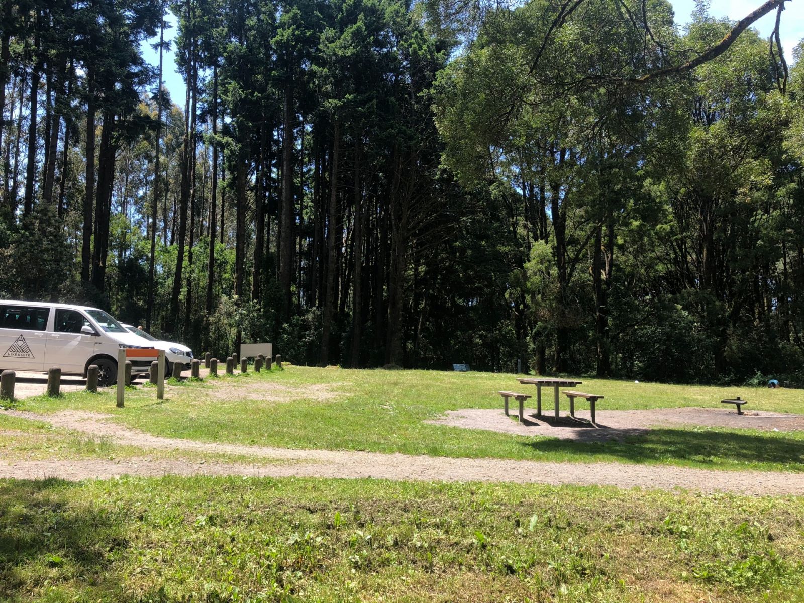 Two vehicles parked next to a grassy campground with a picnic table and fire pit