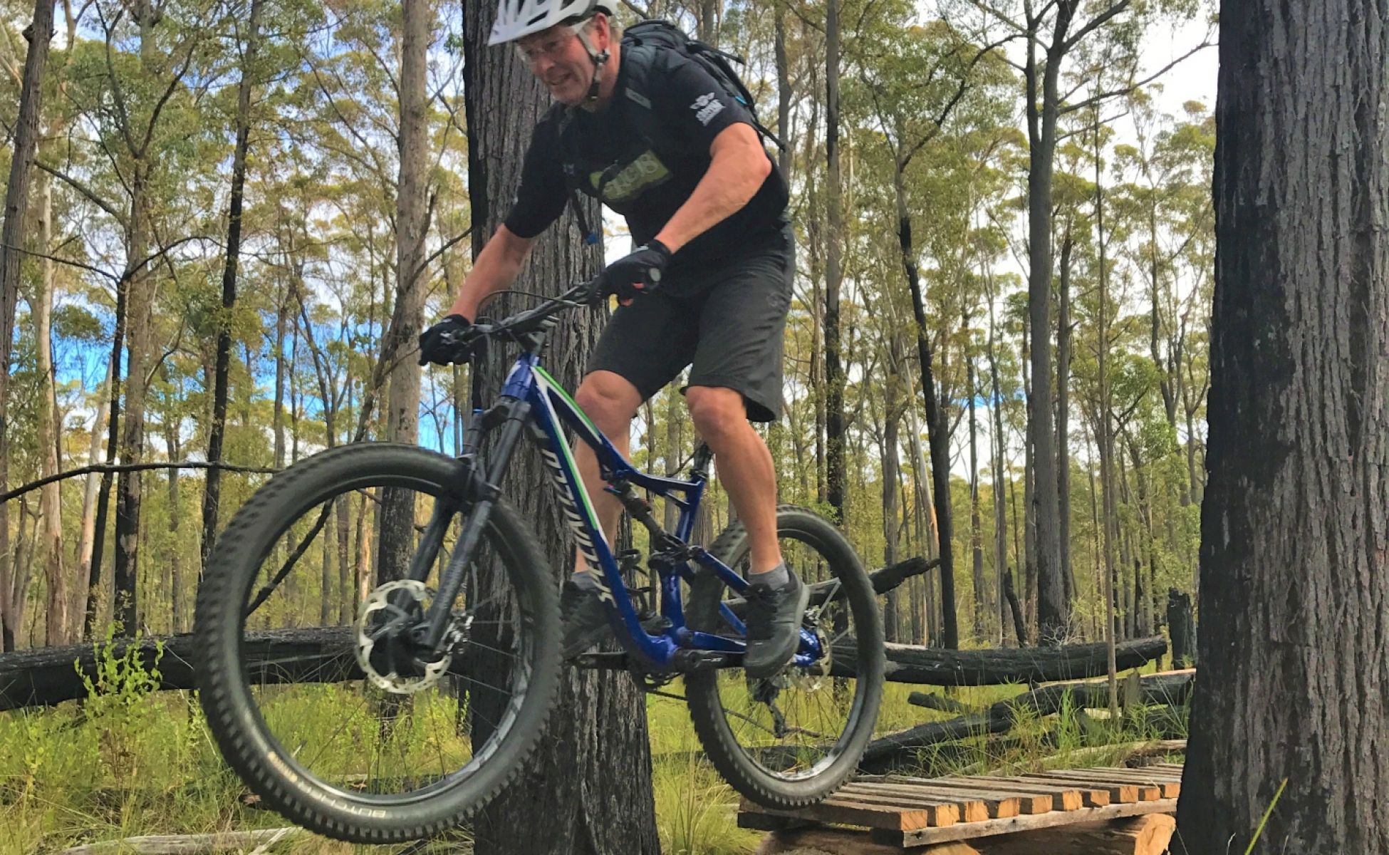 An older man rides a mountain bike over a short jump