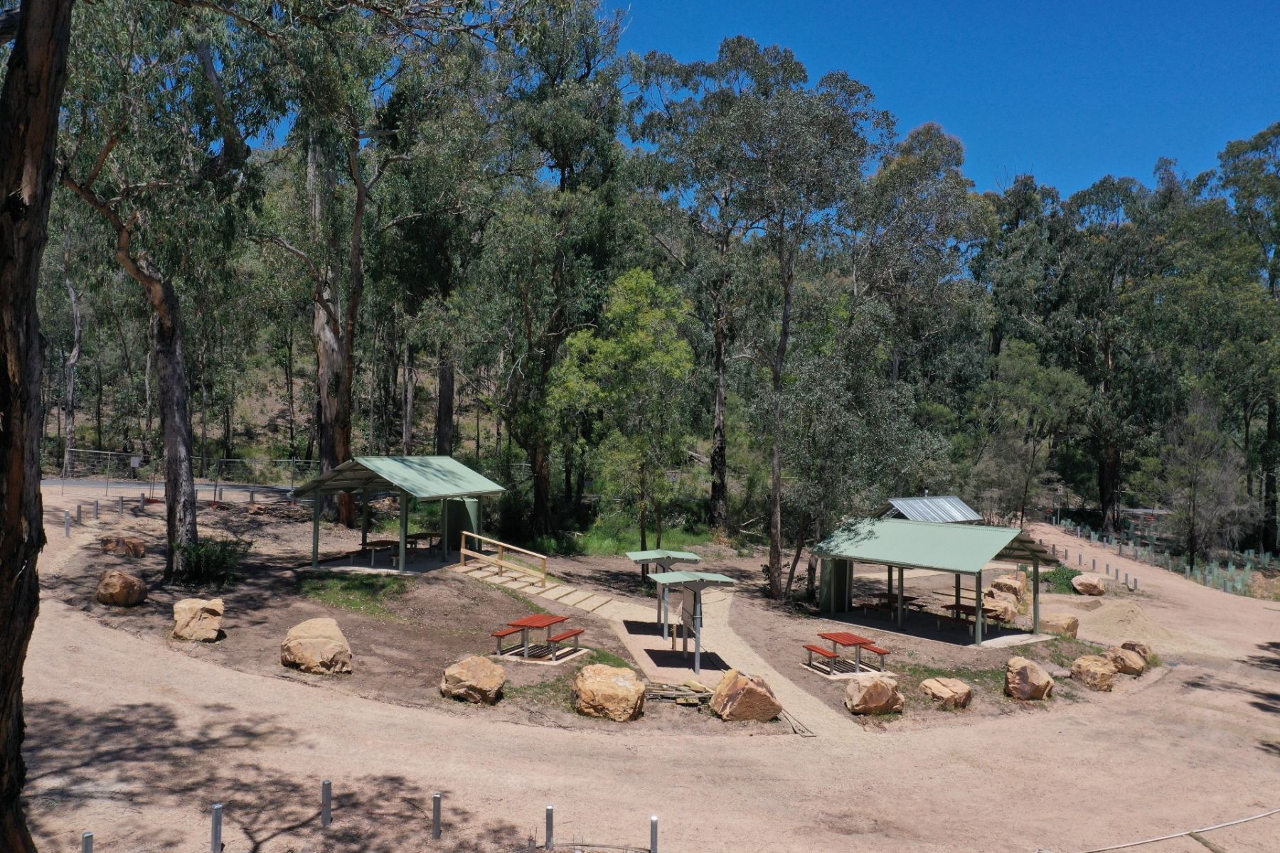 A campground with picnic tables in the open and picnic shelters, with tall trees behind