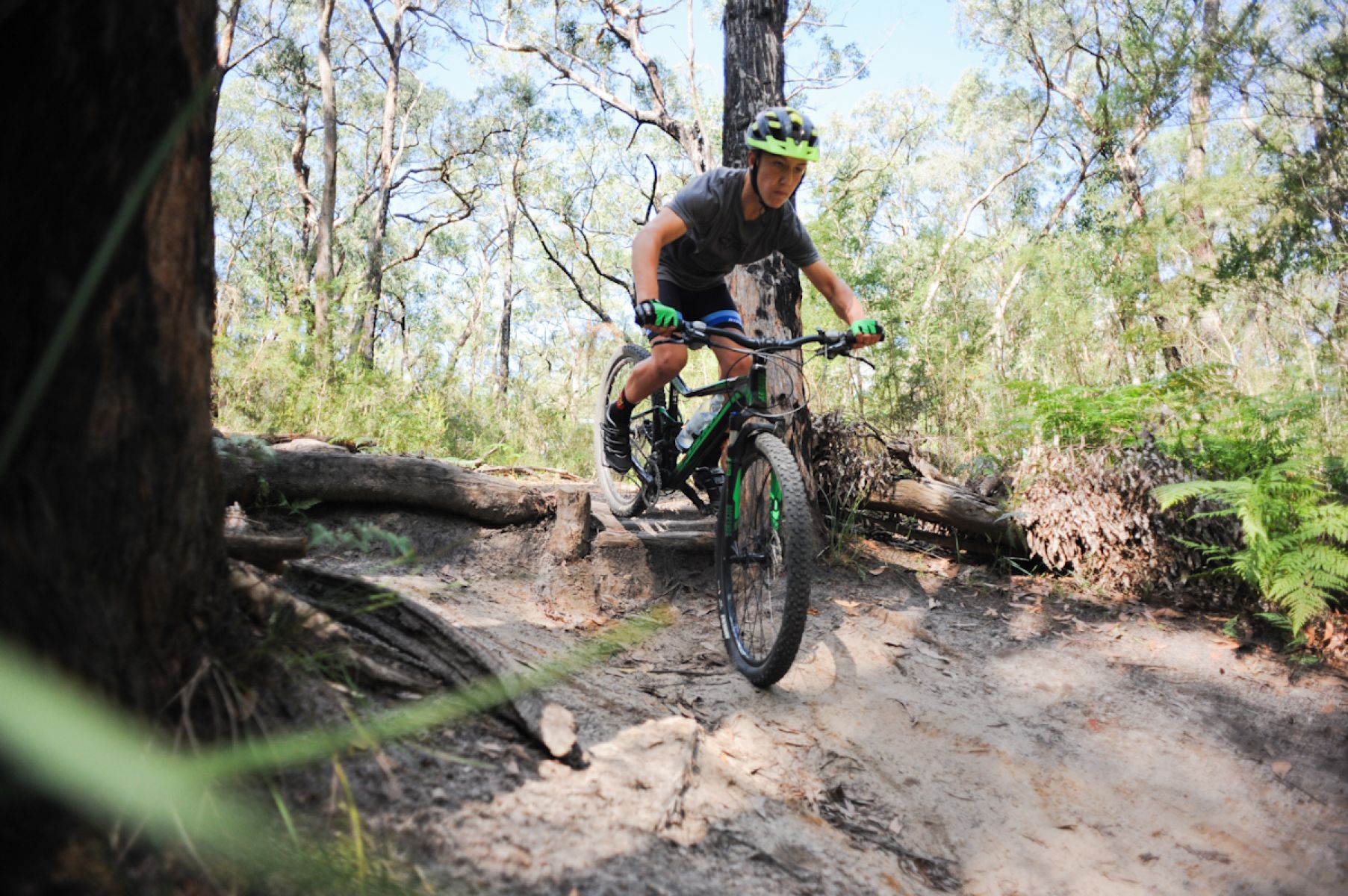 A person rides a mountain bike across a log on a muddy track