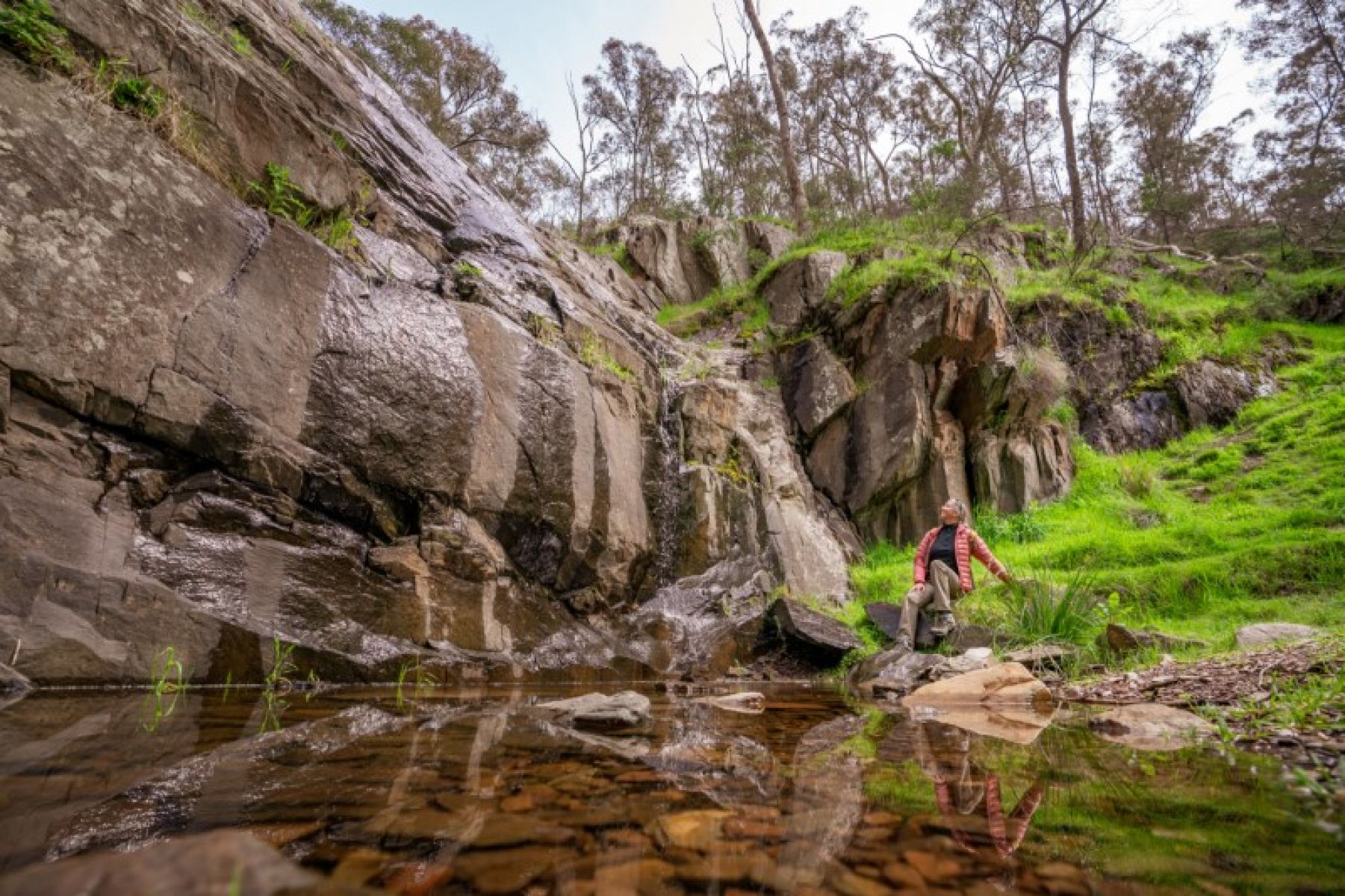 A woman sits beside a pool of water and a waterfall. 