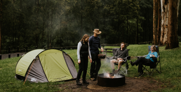 A family sits around a campfire with their tents in the background