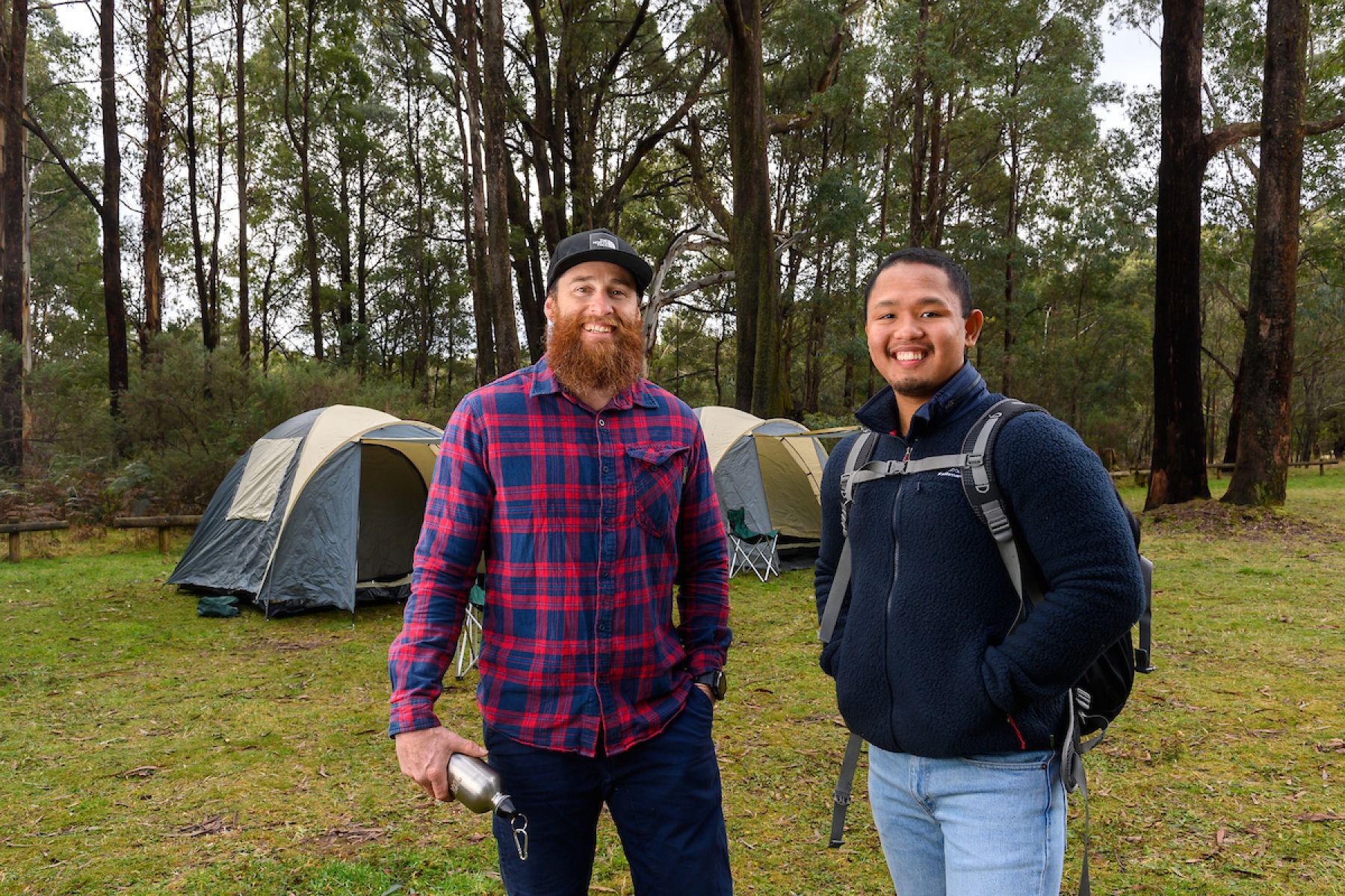 Two friends stand in front of their tents in the bush