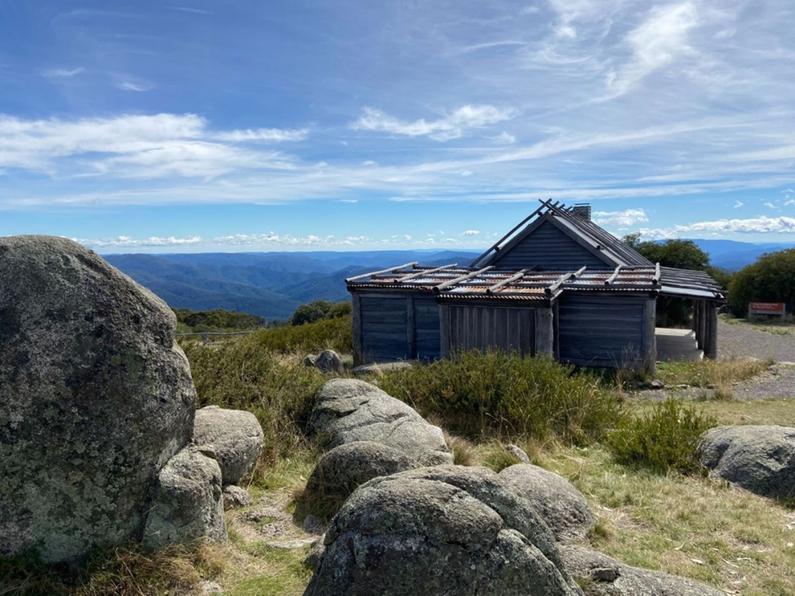 An old timber hut over looking hills in the forest, large boulders in the foreground.