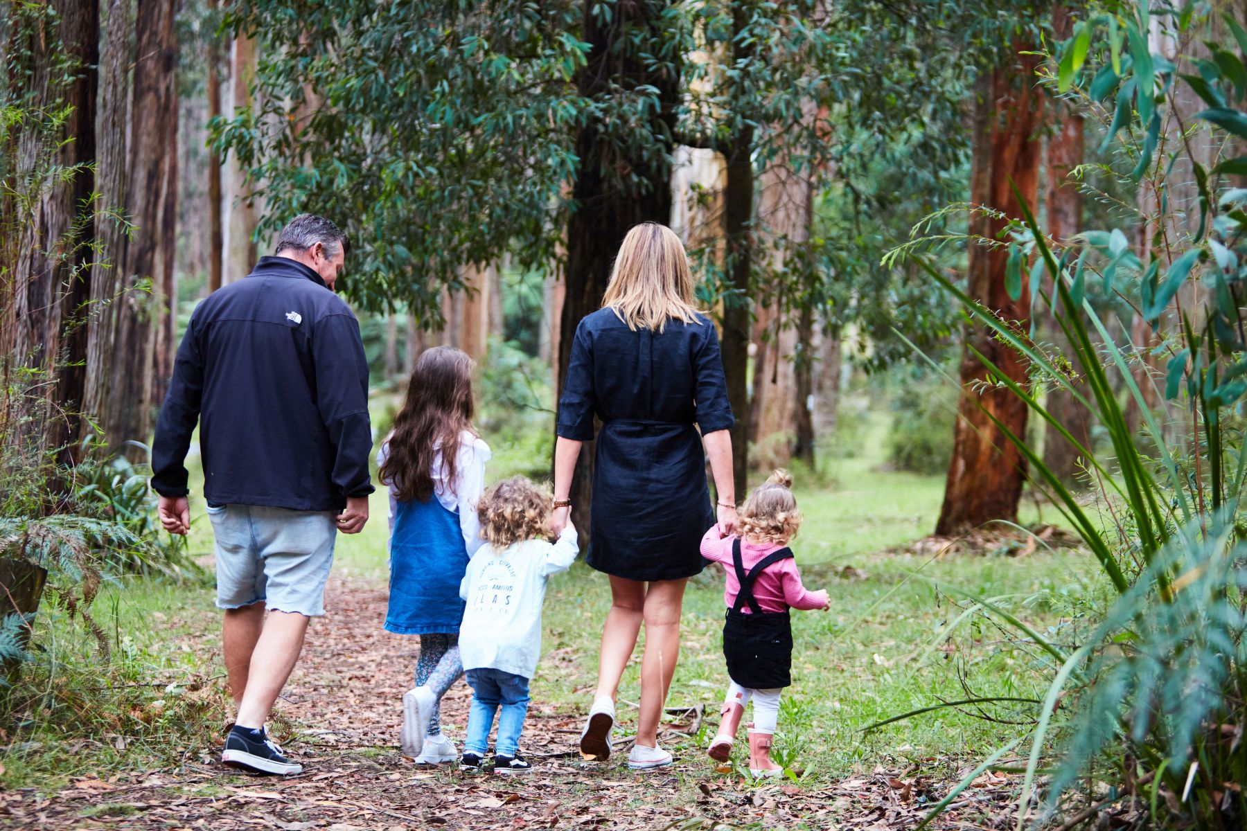 A man, woman and three small children walk through the forest. 