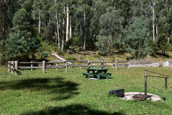 A BBQ fire pit, picnic table and horse yards on a grassy field.