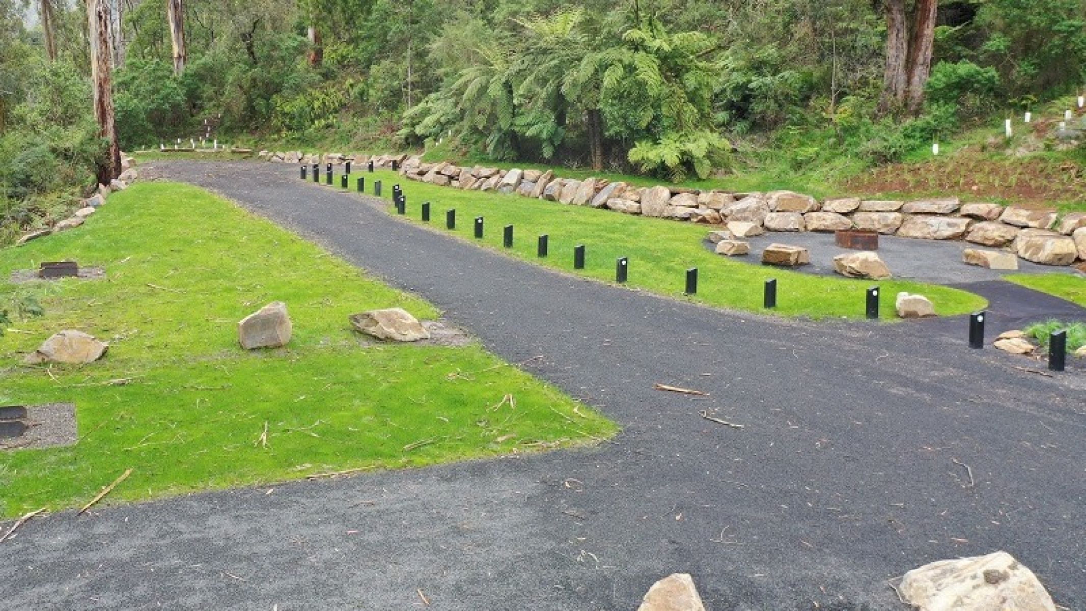 Gravel road and walking track connecting communal fire pit in grassed campground