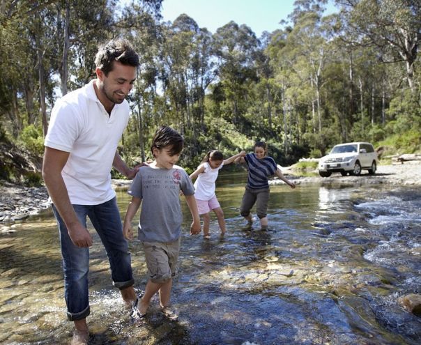 A family of four walking through a river in the forest with their 4WD in the background. 