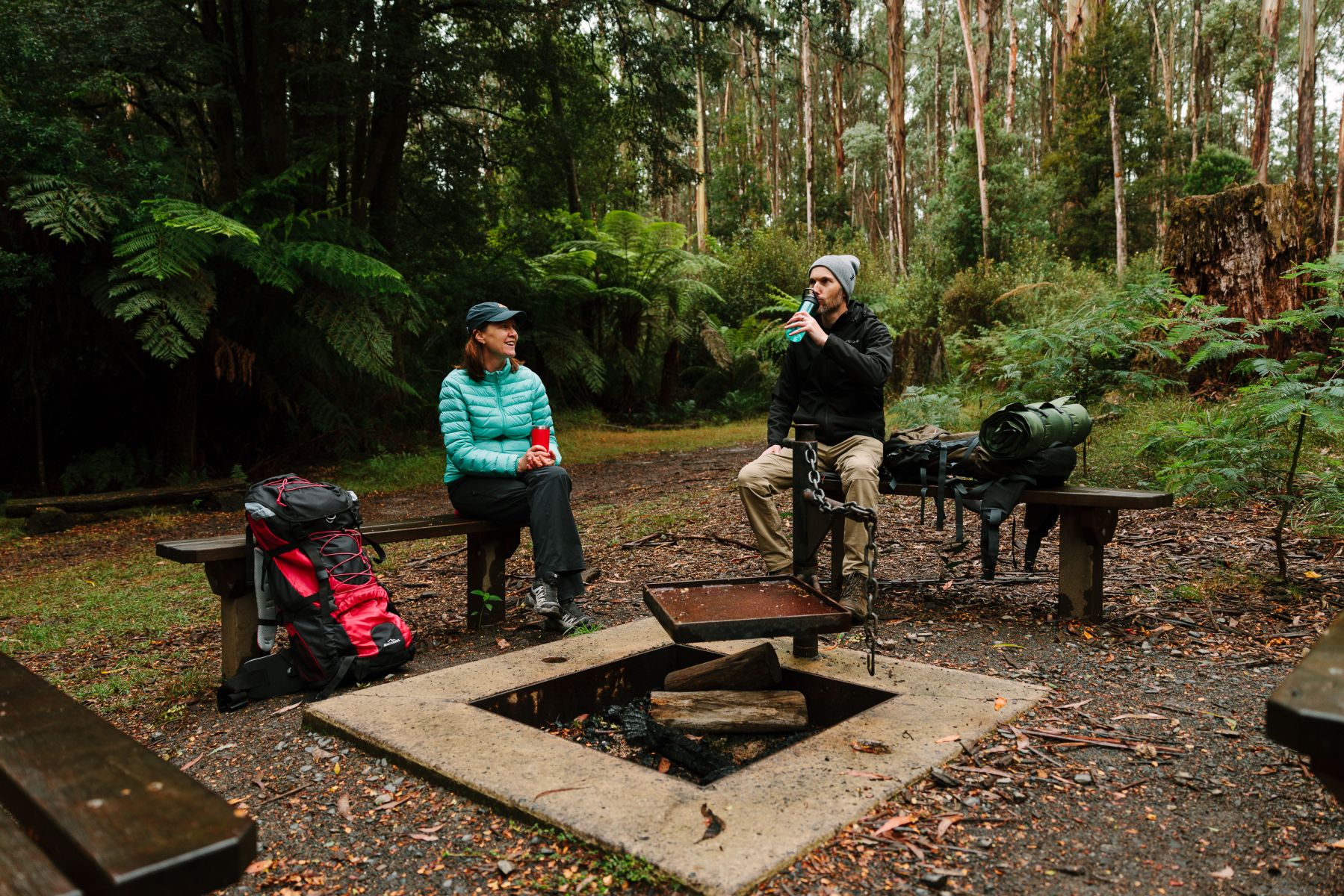 Two people sitting around a fire pit surrounded by forest