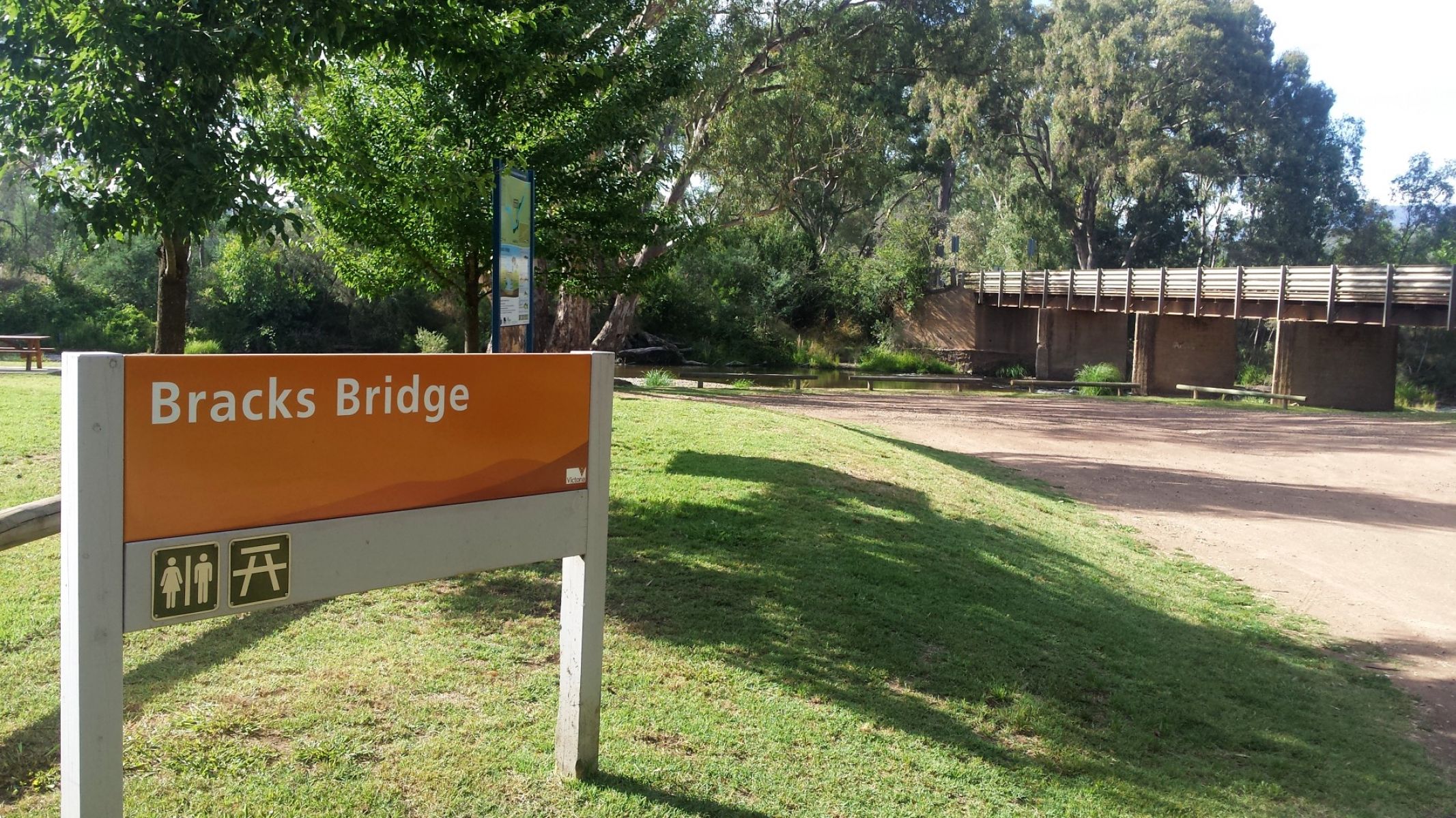 A sign that reads Brack Bridge on a grassy bank with a bridge nearby