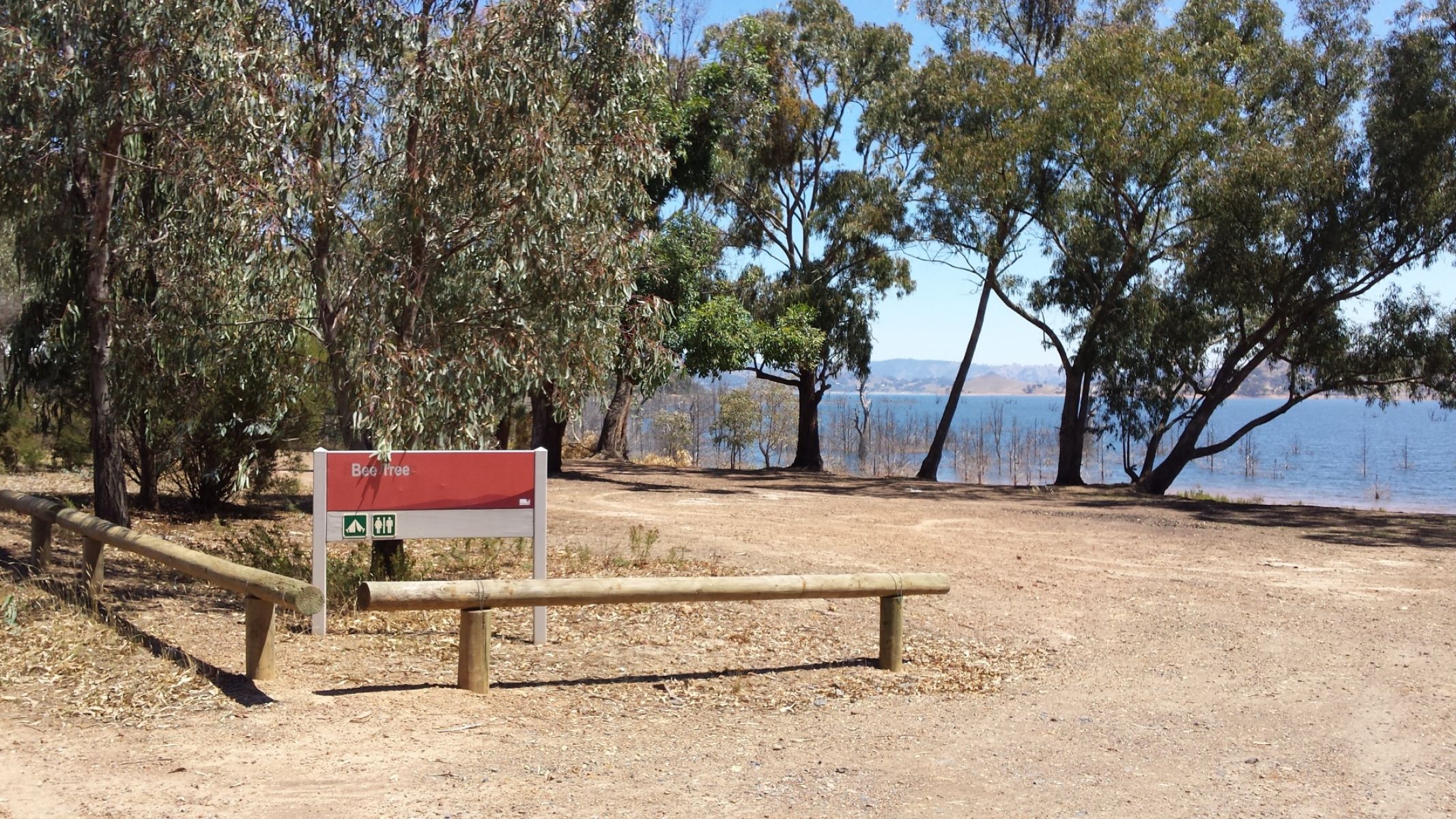 A sign for Bee Tree campground on the ground next to a lake