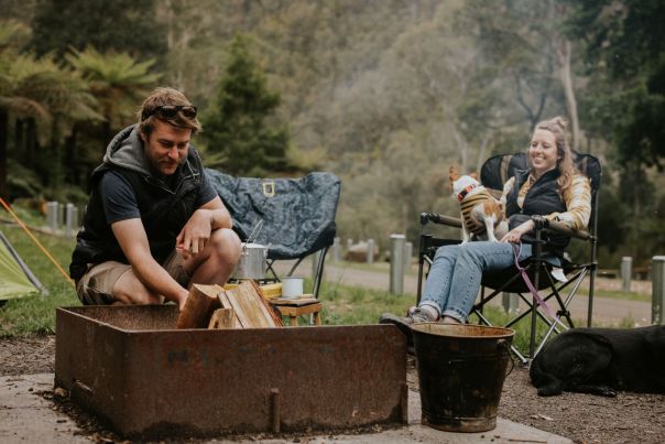 Two people and a dog sitting around a camp fire