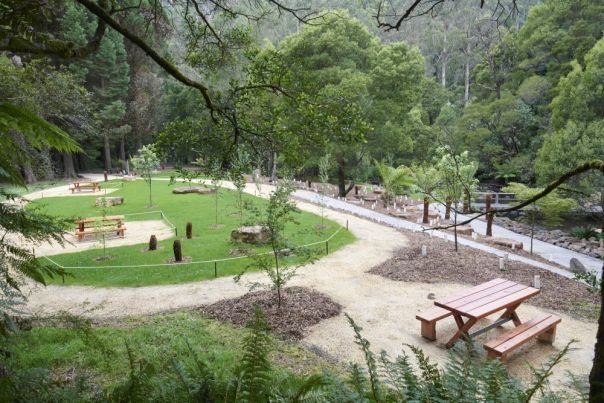 Wooden picnic tables in a grassy area by a shallow river