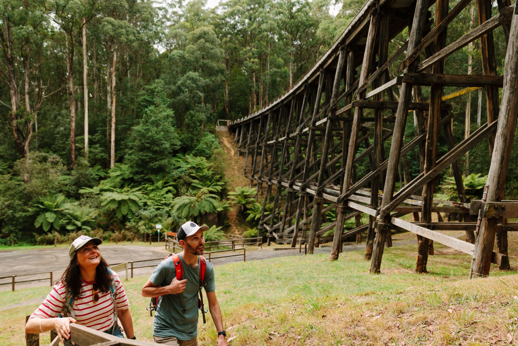 Two people walking towards an old tall wooden bridge