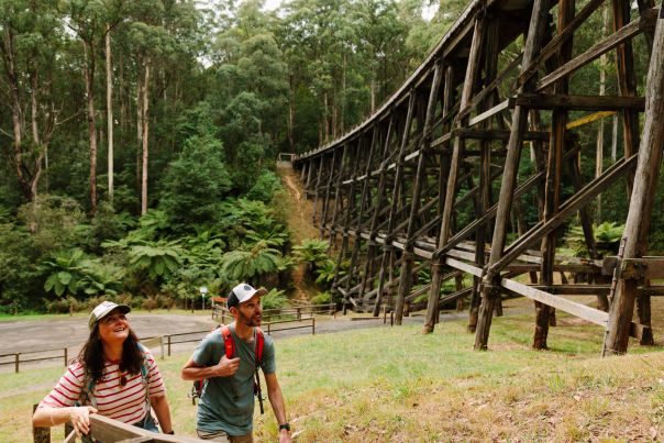 Two people walking towards an old tall wooden bridge