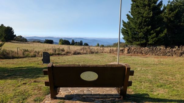 A wooden bench seat on a grassy area overlooking rolling hills in the forest. 