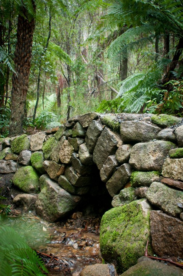 A handcrafted bridge made of large stones that crosses a small stream