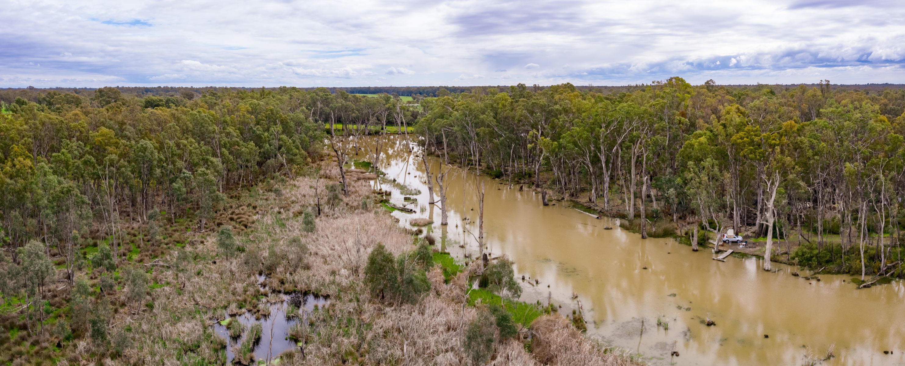 A view form above of a camp set up by a river surrounded by tall trees