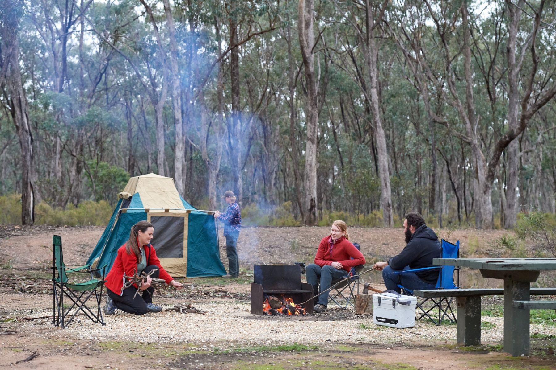 A group of friends sit in front of a tent in the bush.