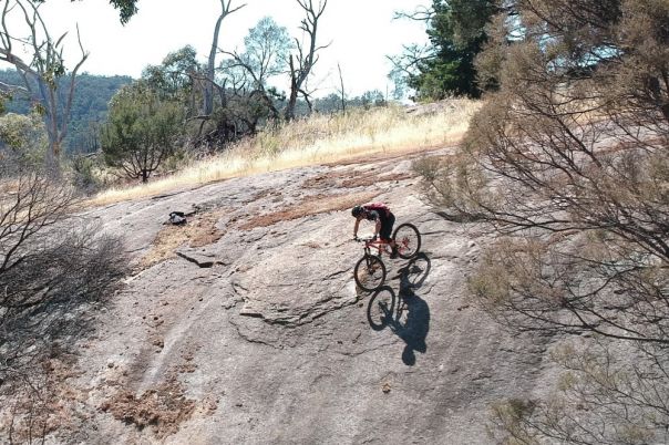 A man rides a mountain bike down a large and steep boulder