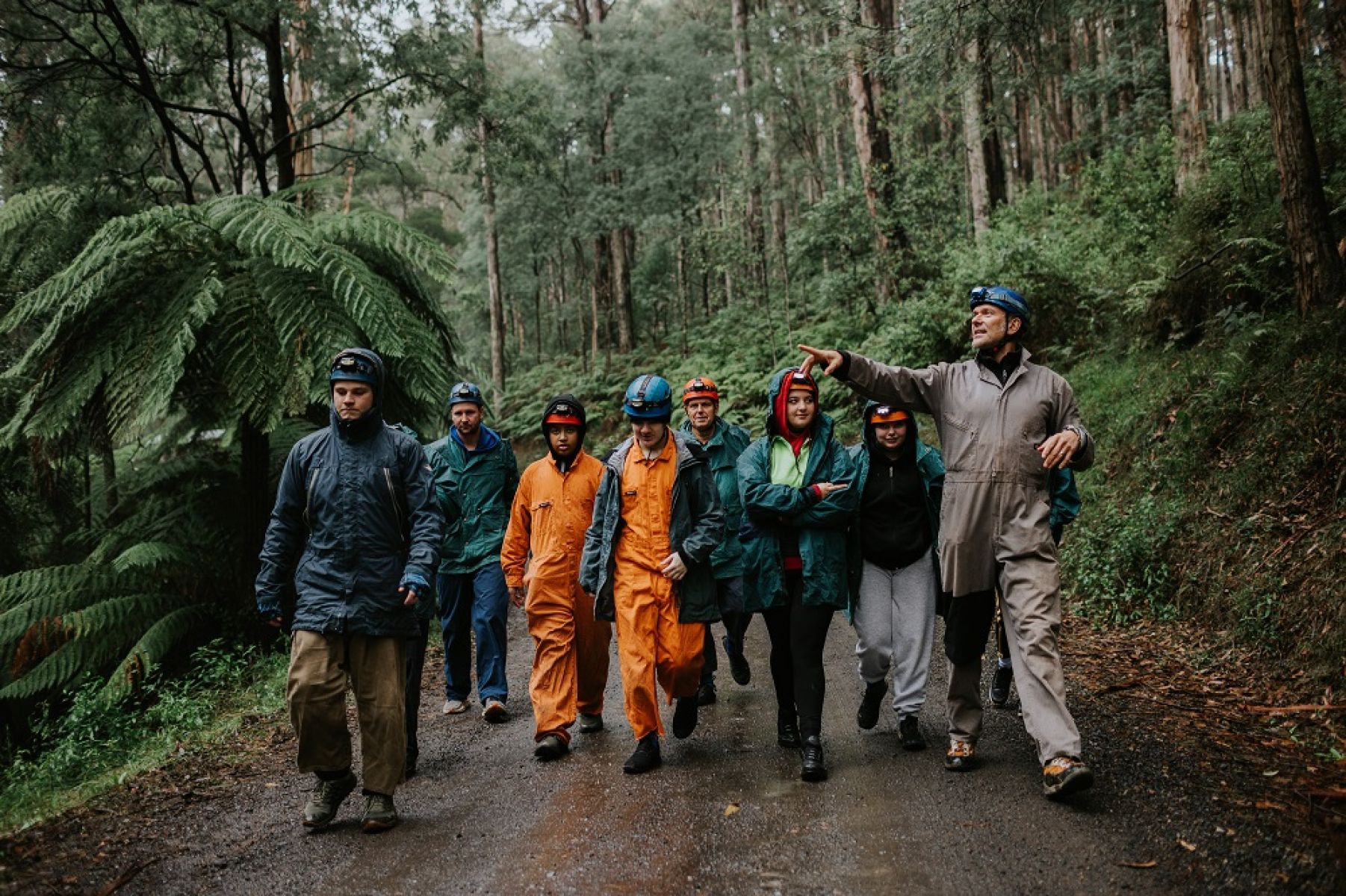 A group of young people in caving gear walking along a forest trail with a guide.