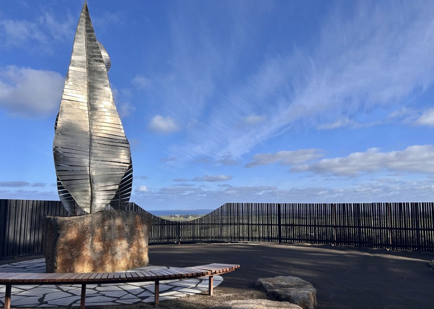 A sculpture surrounded by a stone wall overlooking the ocean. 
