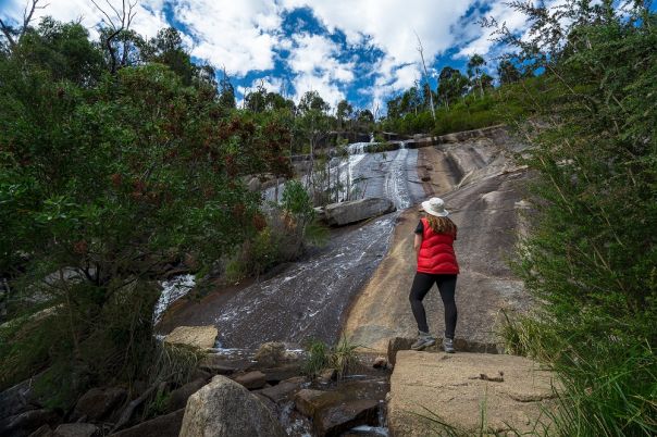 Person standing at bottom of rocky waterfall surrounded by forest