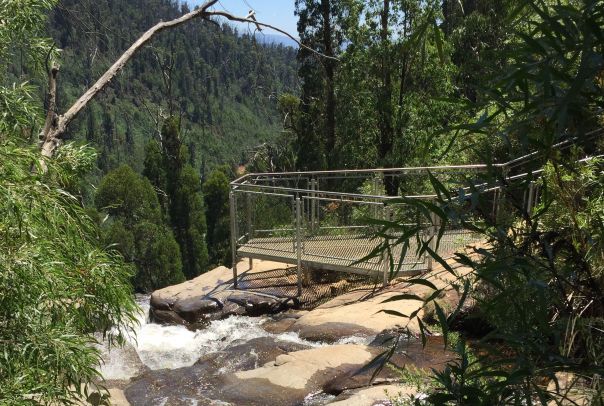 A viewing platform sits on top of a rocky ledge of a waterfall