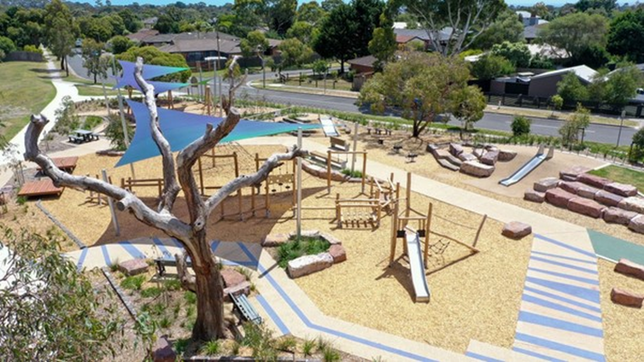 Playground with climbing frame, slide, surrounded by wooden boardwalk. Tree in foreground