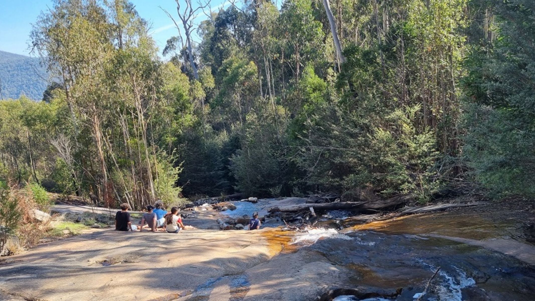 People sitting a rock face overlooking a waterfall in the forest. 