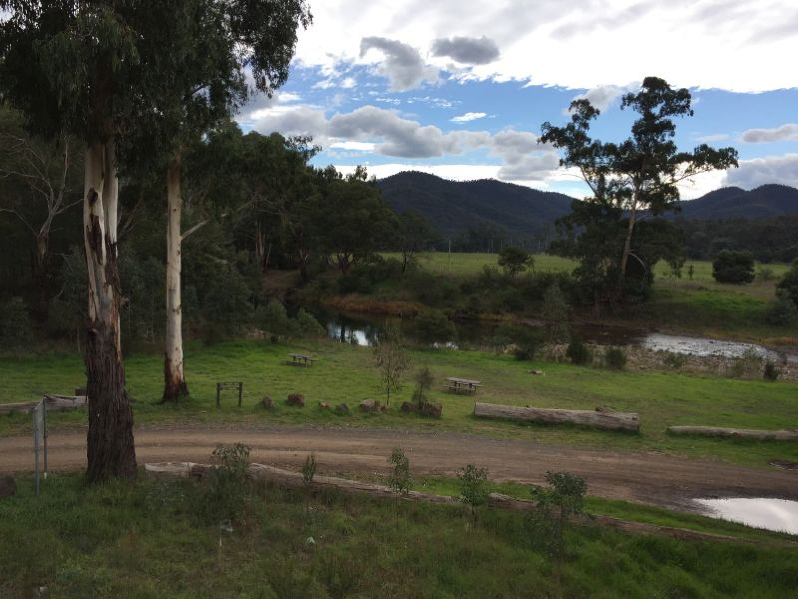 A gravel track running through a grass campground beside a river