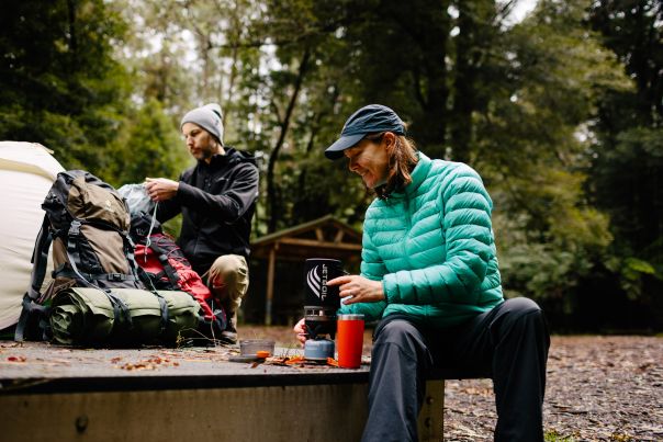 Two people setting up a tent and preparing a drink on a tent platform