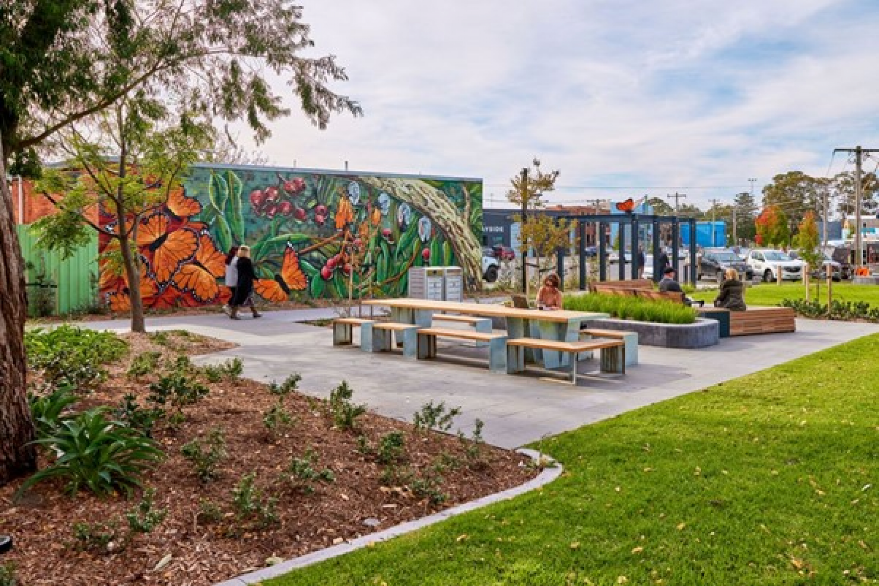 Large wall mural of butterflies in nature centre left, flower beds and grass in foreground, bench seating behind