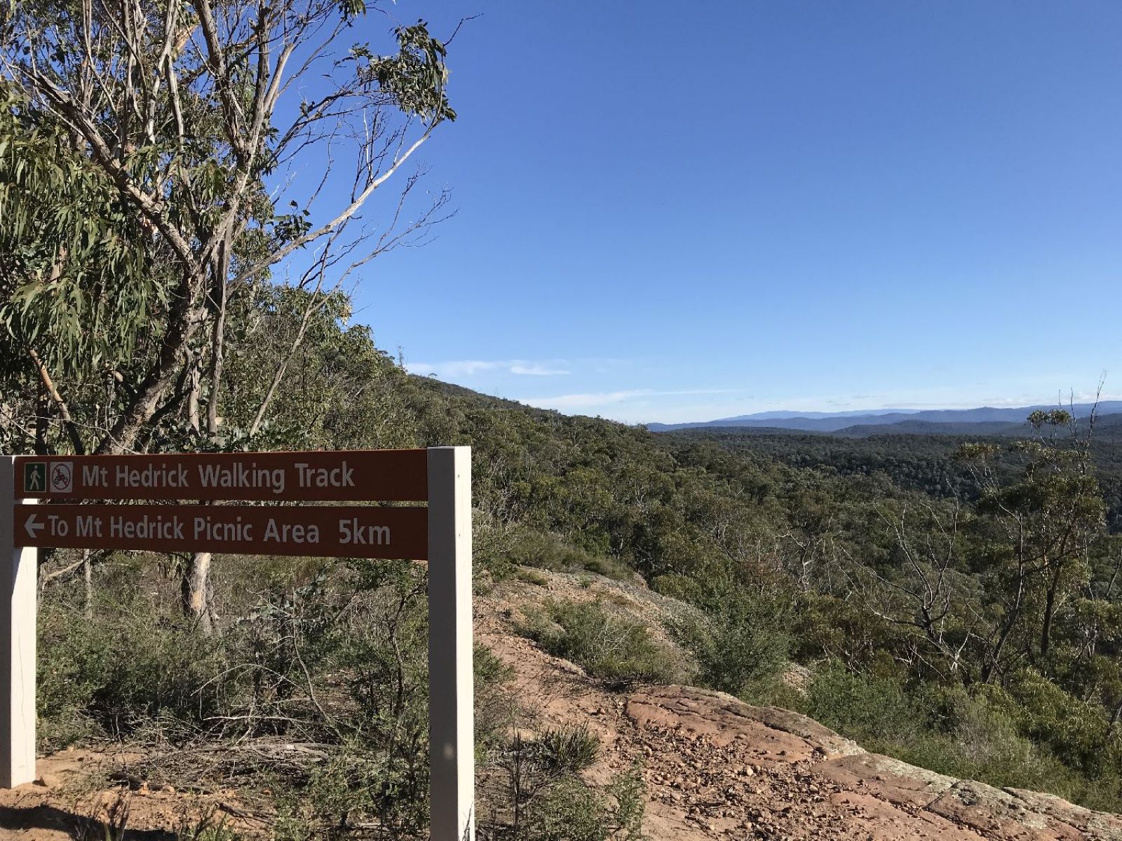 Walking track sign showing the picnic area is 5km away, with a lookout in the background