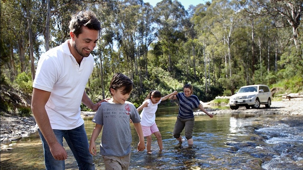 A family standing in a river in the the forest with their 4WD in the background  
