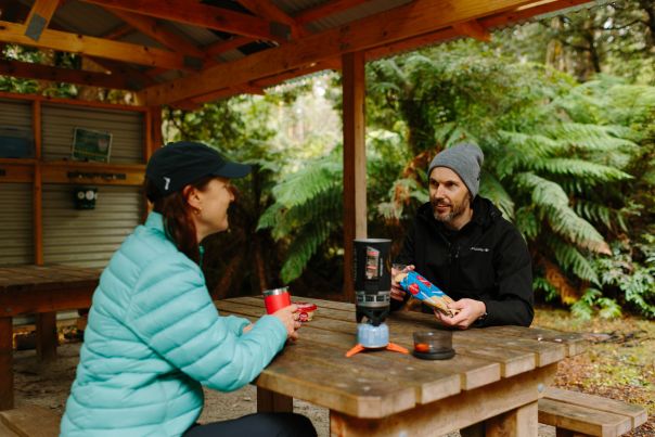 Two people sitting under shelter in the lush forest
