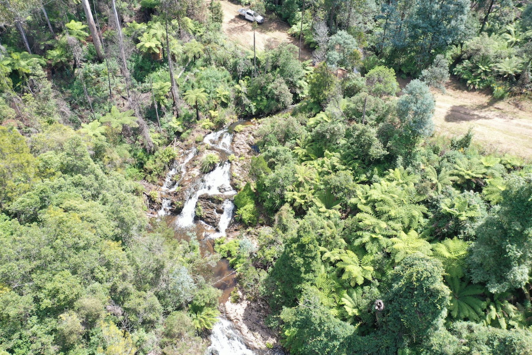 An aerial view of waterfalls running between tall green trees.