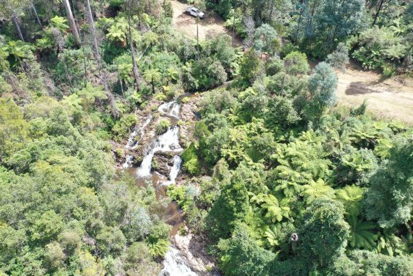 An aerial view of waterfalls running between tall green trees.