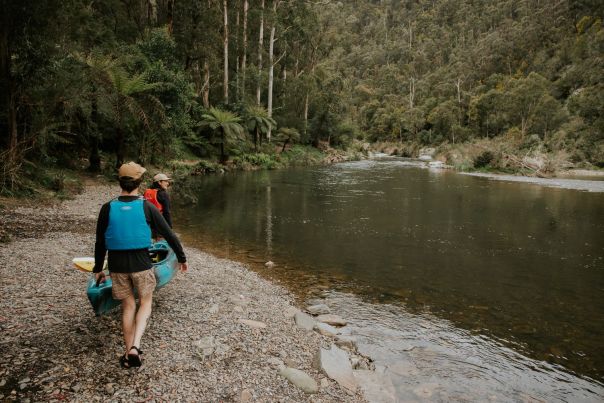 Two people carrying a canoe beside a river