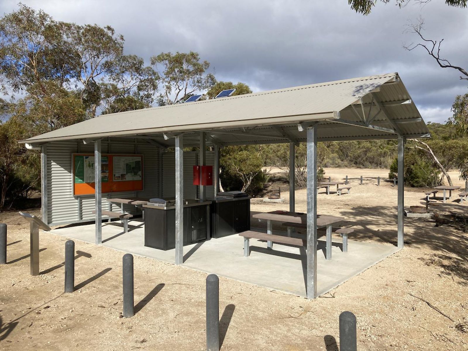 A barbeque and table sit under a metal shelter.
