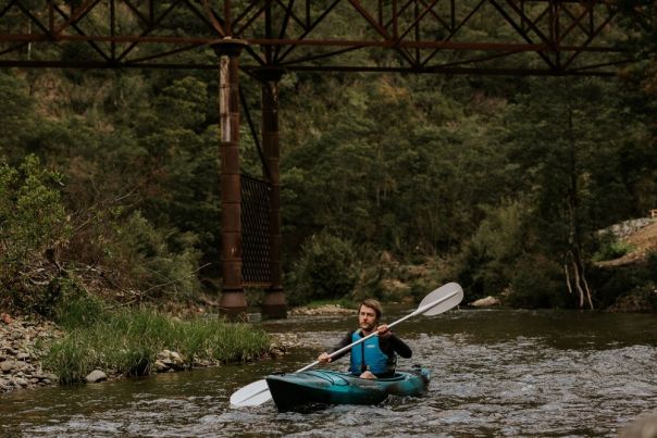 A person kayaking along a river in the forest.