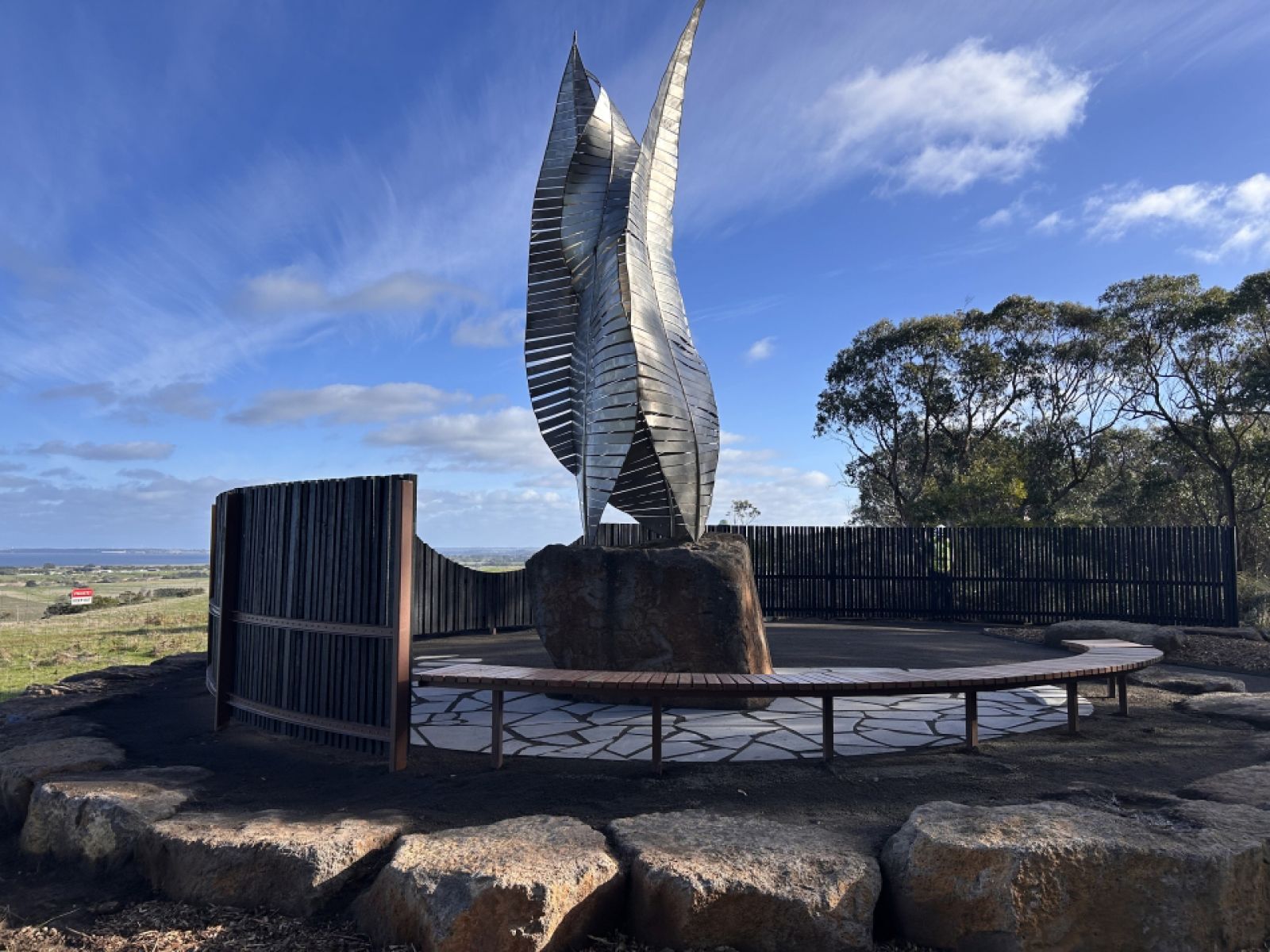A sculpture surrounded by a stone wall overlooking the ocean.