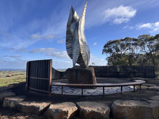 A sculpture surrounded by a stone wall overlooking the ocean.