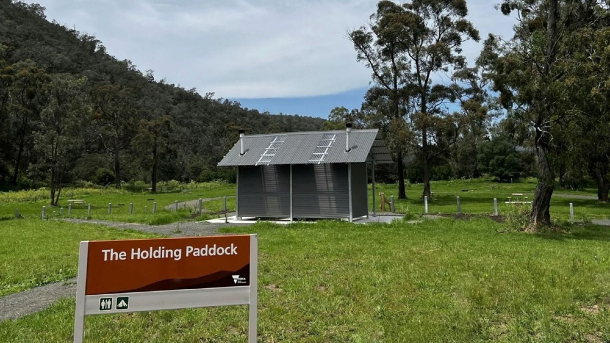 A grassy campground with a toiilet facility and a sign