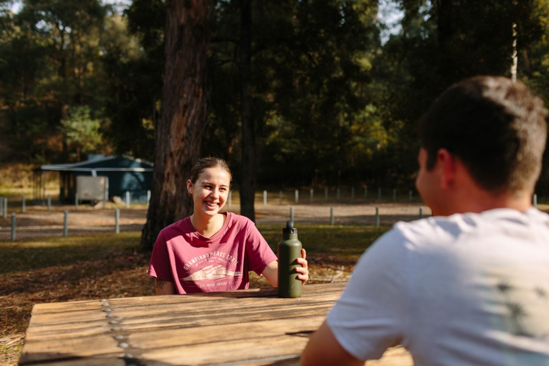 Two people at a picnic table with hut in background