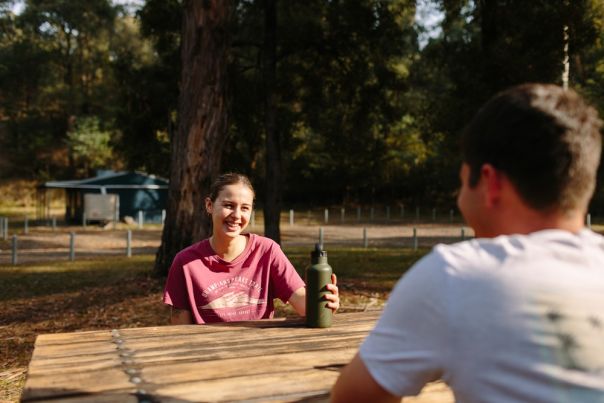 Two people at a picnic table with hut in background