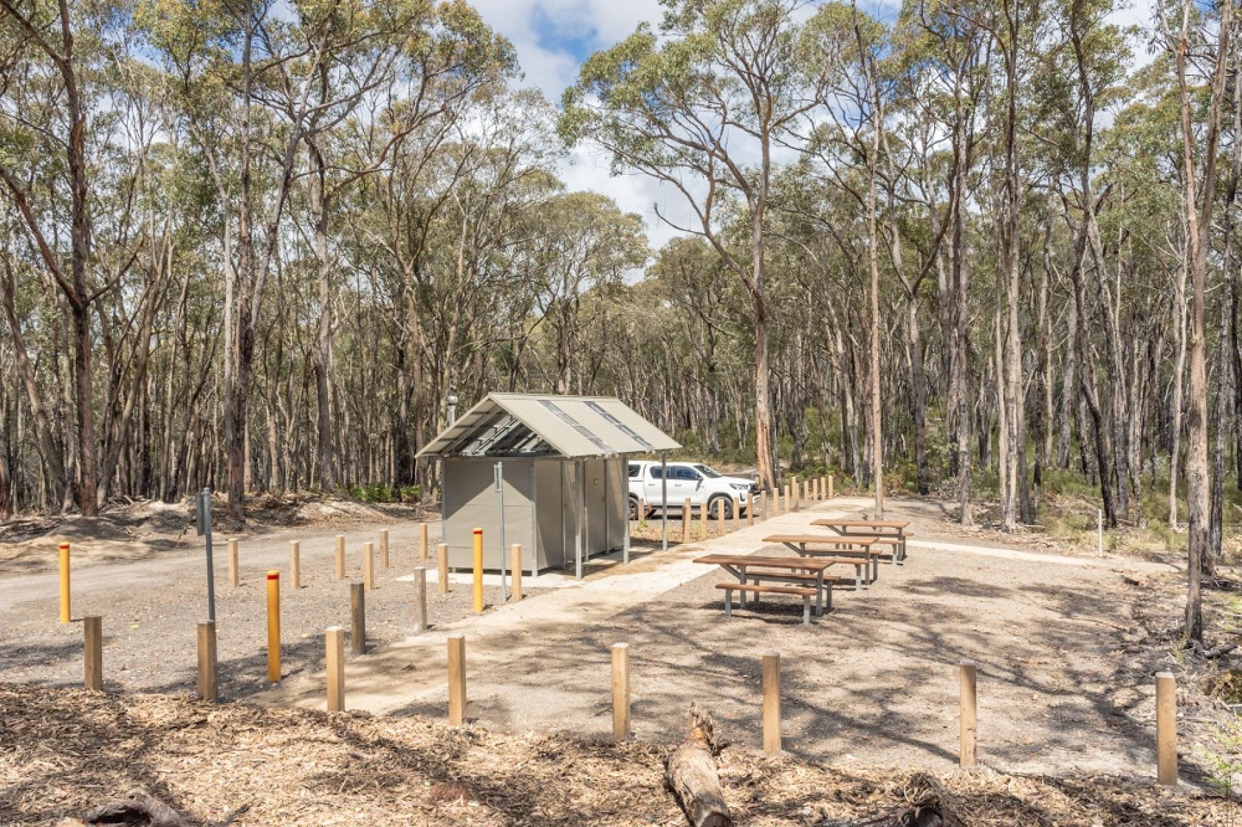 A metal accessible toilet block with large picnic tables behind it in a bushland clearing. 