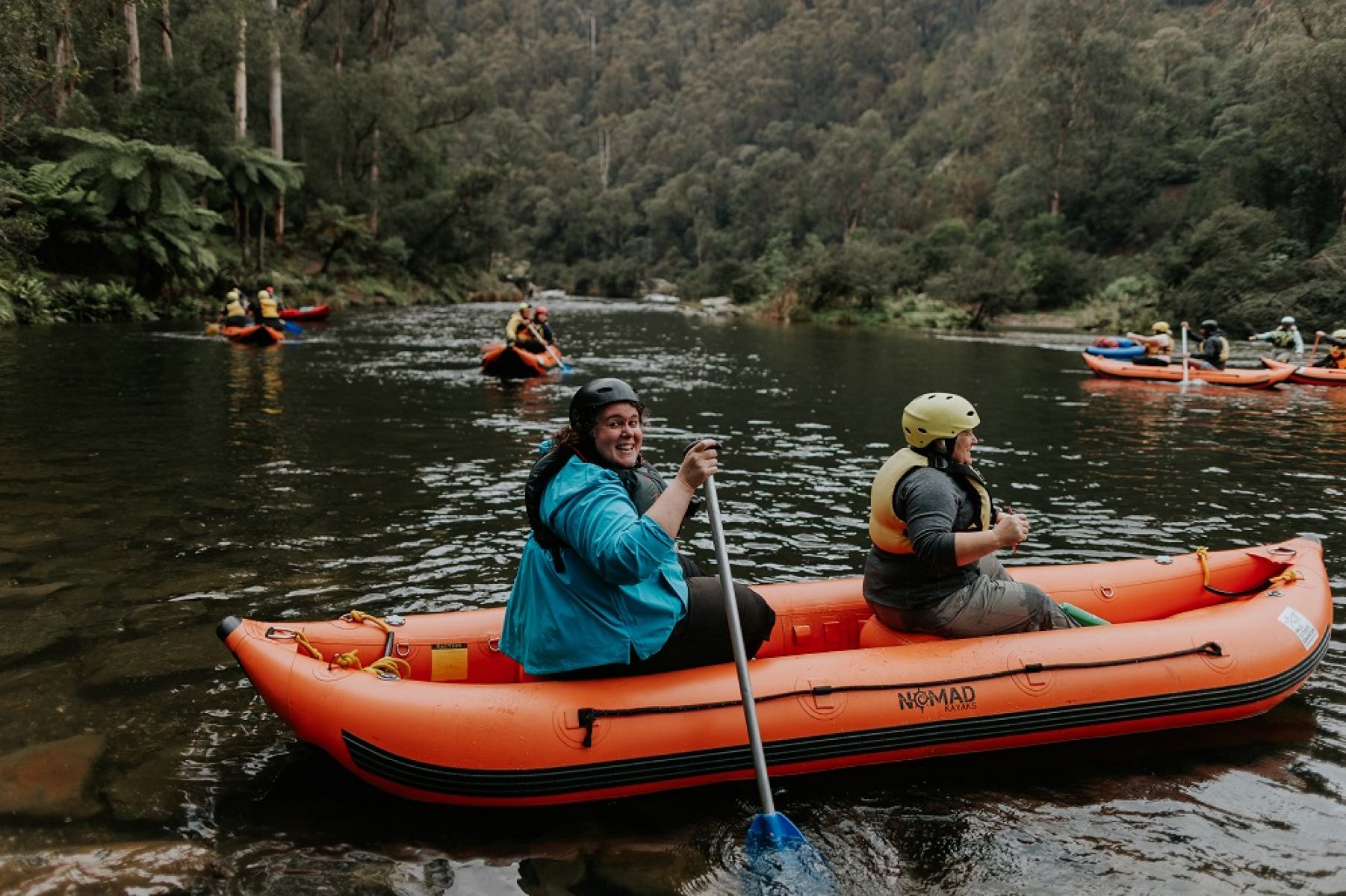 People canoeing in multiple canoes on a river surrounded by forest