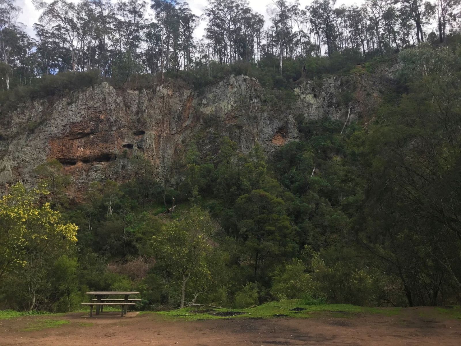 A picnic table with towering rocky terrain in the background and thick green bushland.