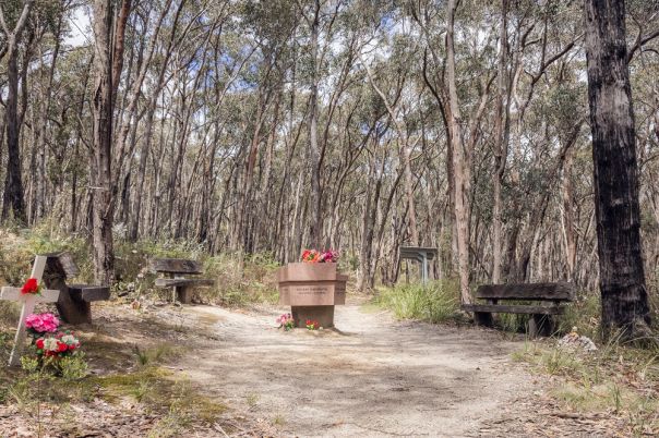 A brown stone memorial with flowers on top displays the names of 5 firefigthers who lost their lives in bushfires in 1998.
